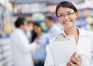 A long term care pharmacist smiles and holds a clipboard.
