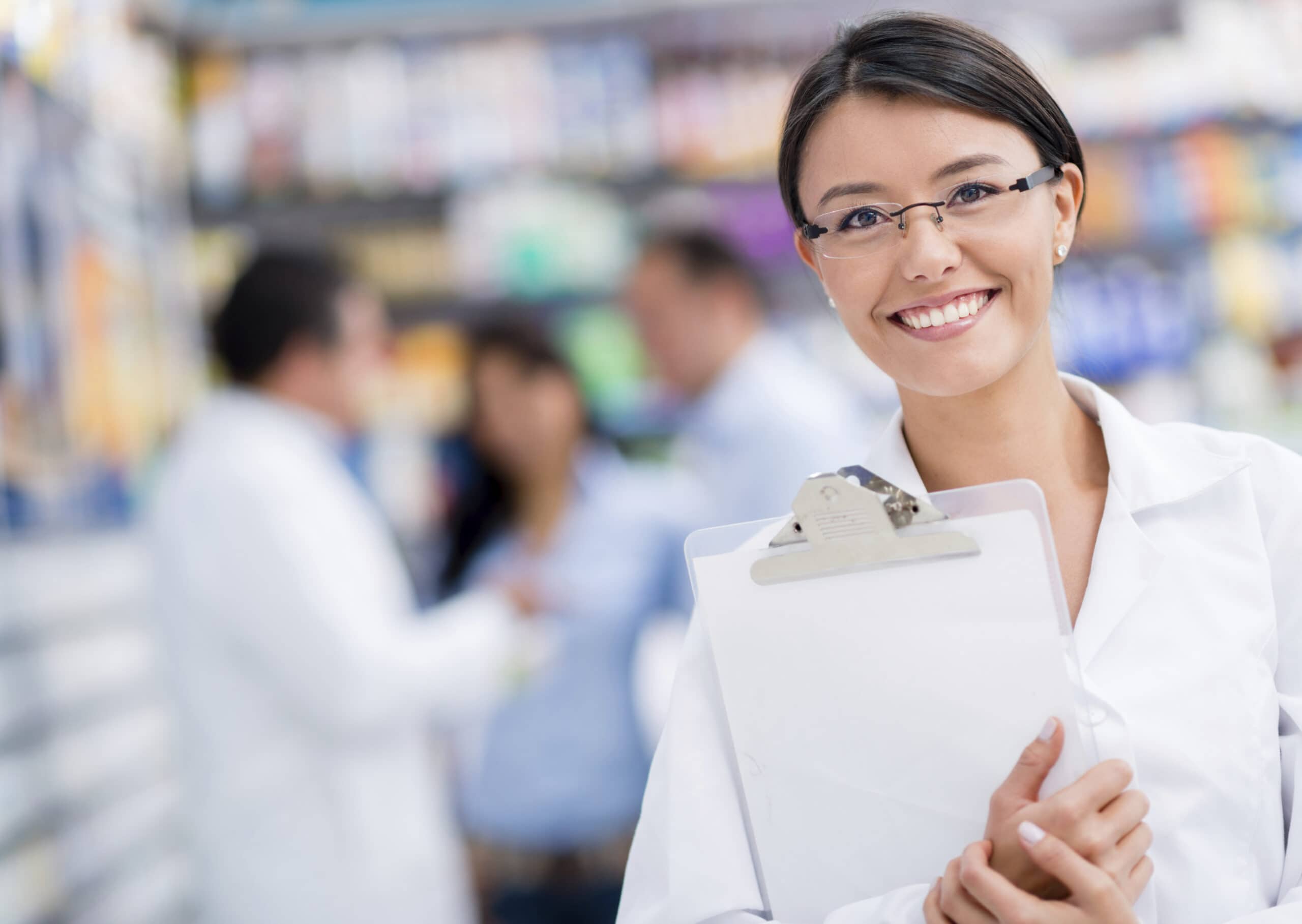 A long term care pharmacist smiles and holds a clipboard.